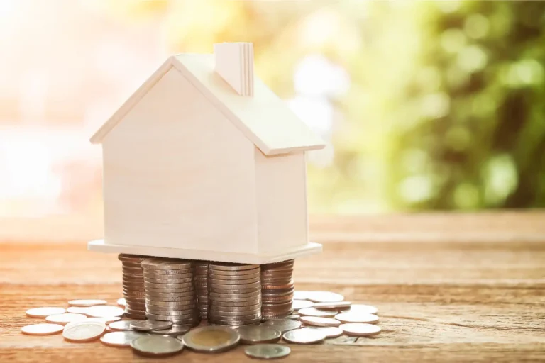 Vivienda apoyada sobre monedas que representa la gestión legal de una sociedad patrimonial inmobiliaria